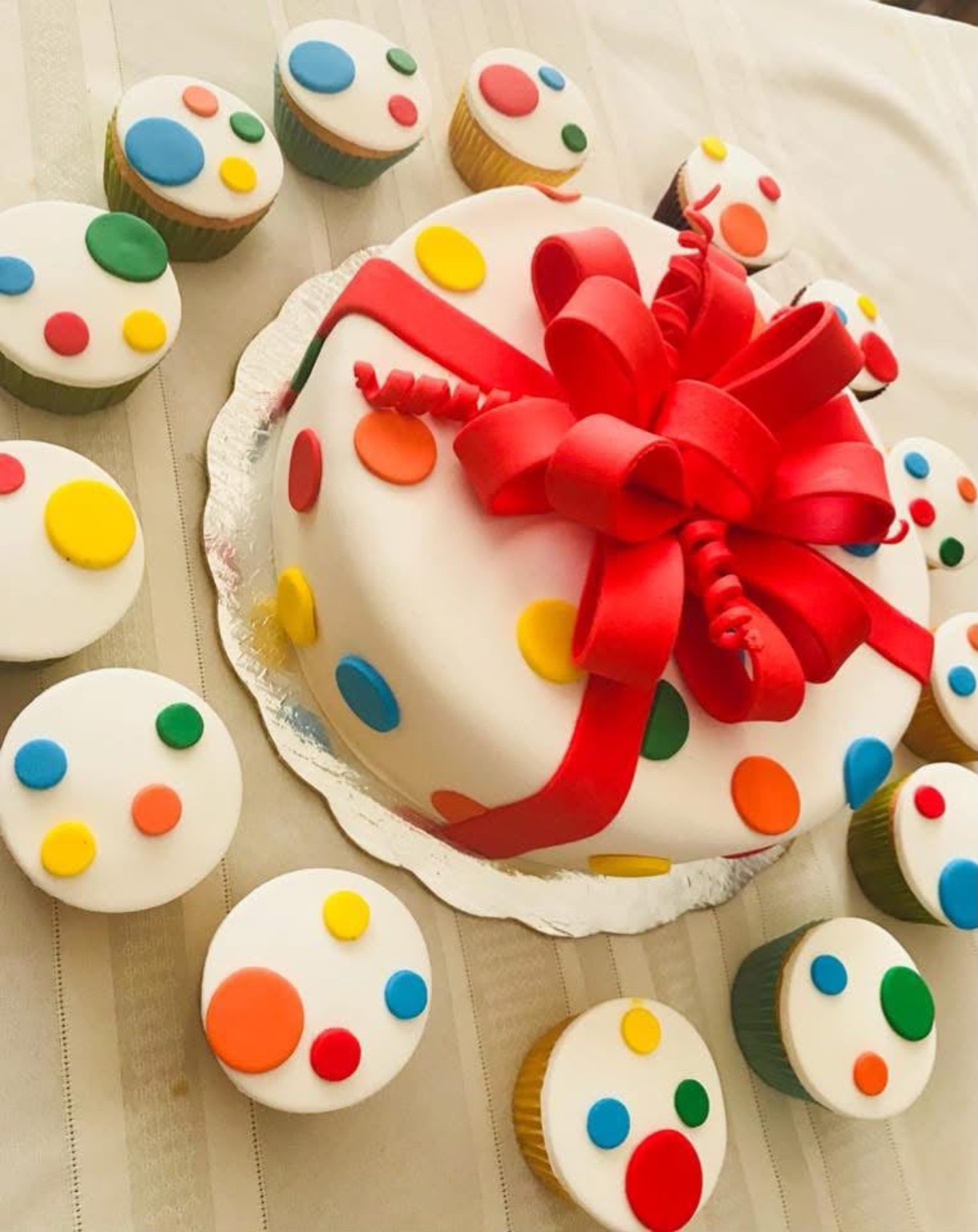 Queque blanco con lazo rojo y cupcakes decorados con puntos de colores